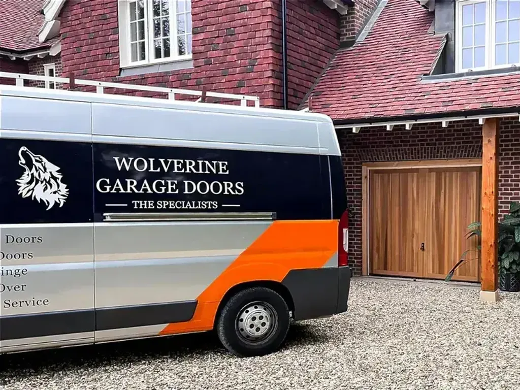 A Wolverine Garage Doors van parked on a driveway beside two new timber garage doors
