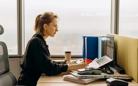 An accountant working at a desk with a laptop, calculator and document folders