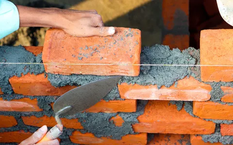 Builder laying a brick onto fresh mortar with a trowel while building a wall
