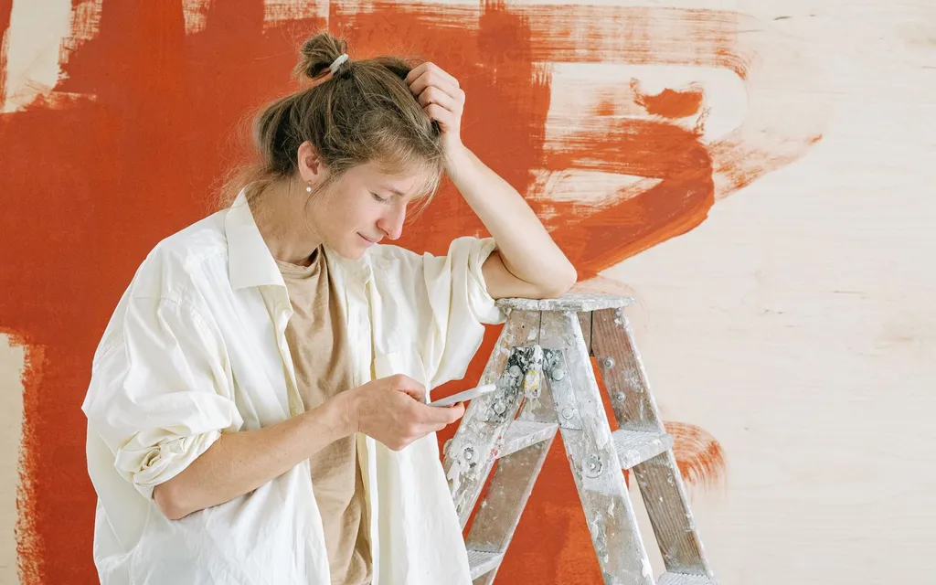 A decorator by a stepladder checking a phone in front of a half-painted wall