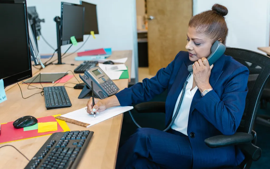 A hotel front-desk agent on the phone at reception with a screen in front of them