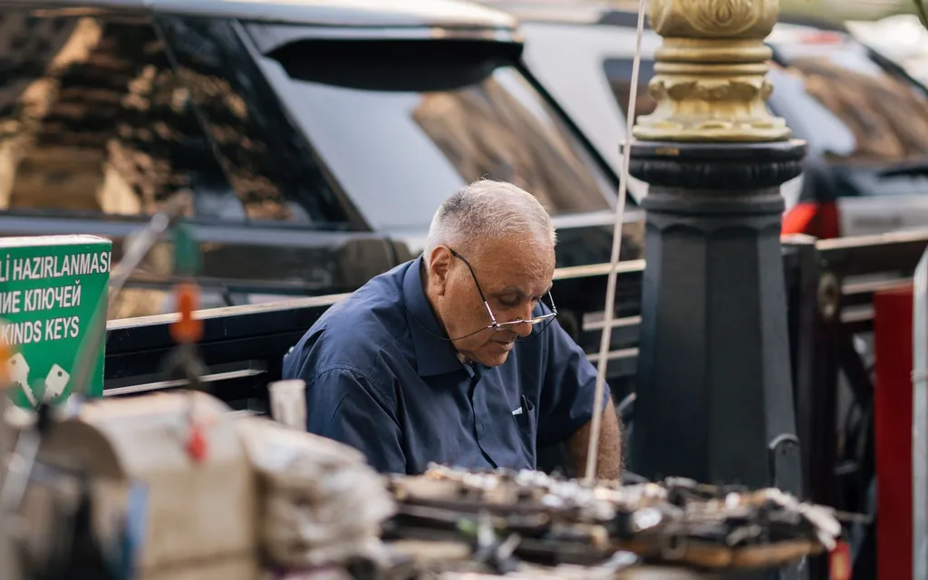 An elderly locksmith working with keys at a street key-cutting stall