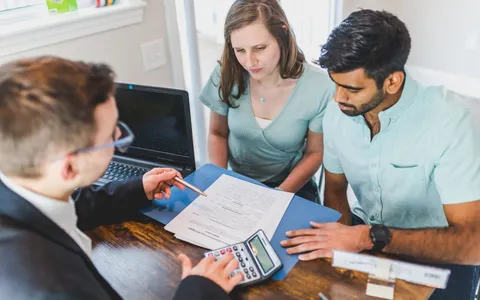 Mortgage adviser pointing at a loan application while a couple review it across a desk