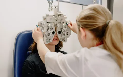 Optometrist adjusting a phoropter while testing a patient's vision during an eye examination