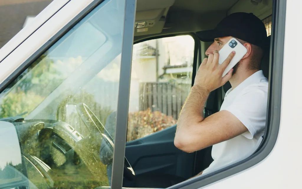 Plumber taking a call on a mobile phone in his work van
