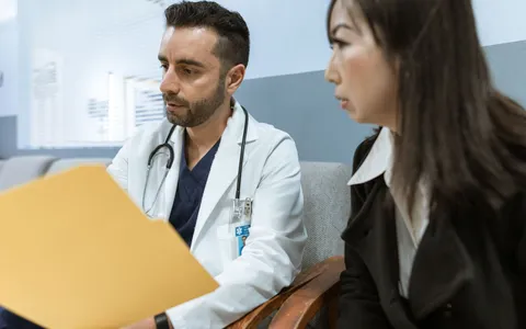 A private GP with a stethoscope reviewing notes with a patient in a clinic consultation
